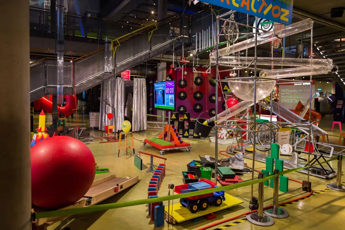 Futuristic green ship-shaped NEMO building beside the water, with families climbing to its panoramic rooftop terrace.