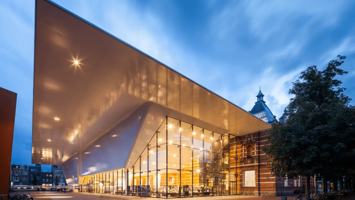Modern white bathtub-shaped façade of the Stedelijk Museum with people gathering outside on Museumplein.