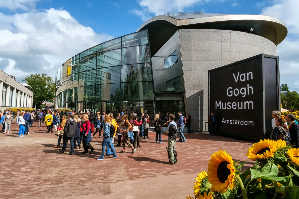 Exterior of the Van Gogh Museum at Museumplein, modern glass building surrounded by art lovers and bicycles.